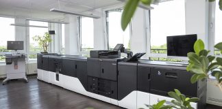 Kyocera TASKalfa Pro 15000c: tutta la potenza della stampa in bobina dentro una macchina a foglio Kyocera TASKalfa Pro 15000c installata in un reparto stampa professionale, con unità inkjet a foglio e finitura inline, in un ambiente luminoso con piante e ampie finestre